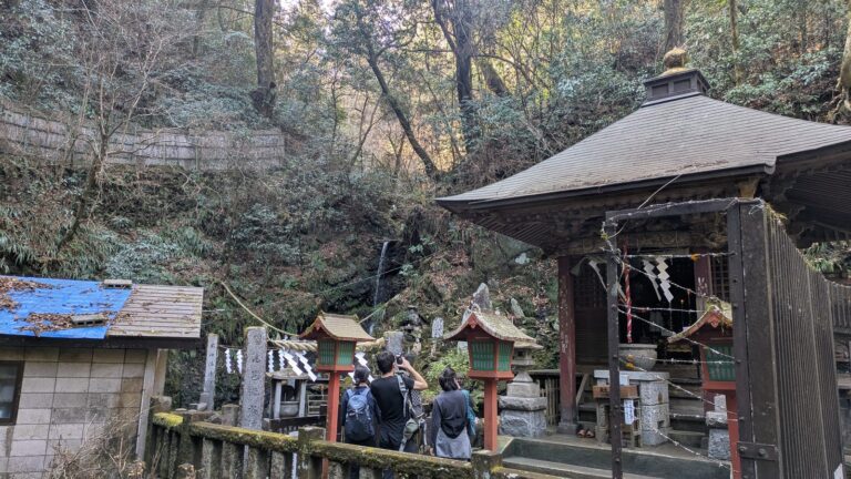 A small waterfall behind a wooden shrine building on Trail 6