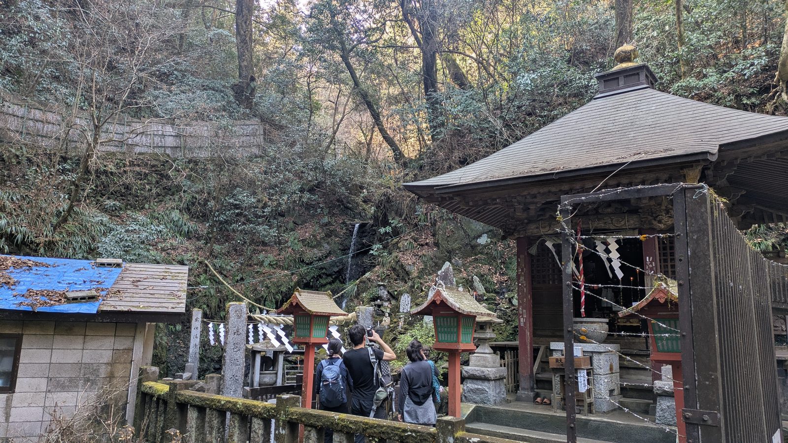 A small waterfall behind a wooden shrine building on Trail 6