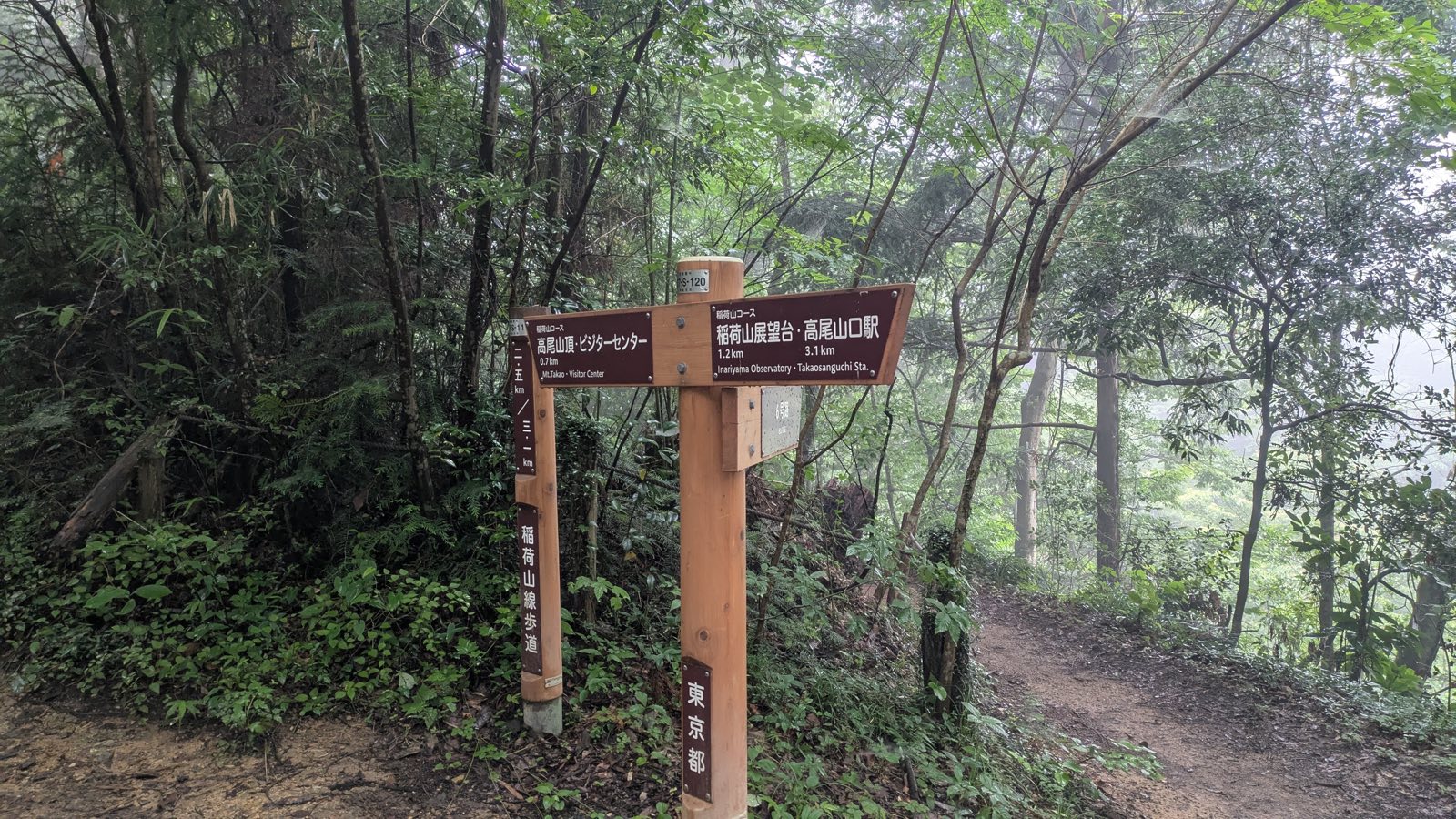 A bilingual wooden signpost on the Inariyama Trail giving distances to the summit, the observatory, Takaosanguchi Station