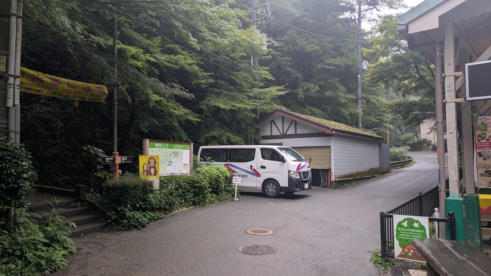 The entrance to the Inariyama Trail beside a green trail noticeboard, with stone steps leading up to the left of the cable car base station