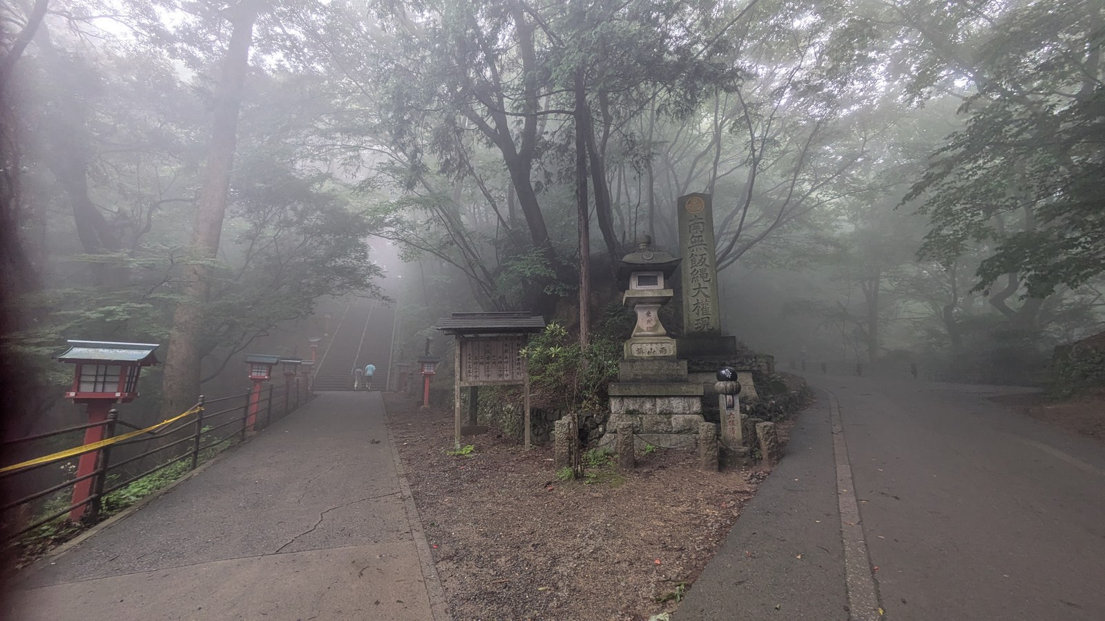 A misty fork where a stone staircase climbs to the left and a paved road curves away to the right