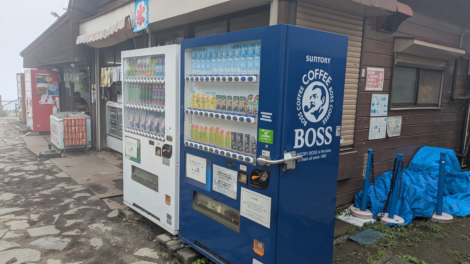 Two drinks vending machines beside a wooden shop building at the summit