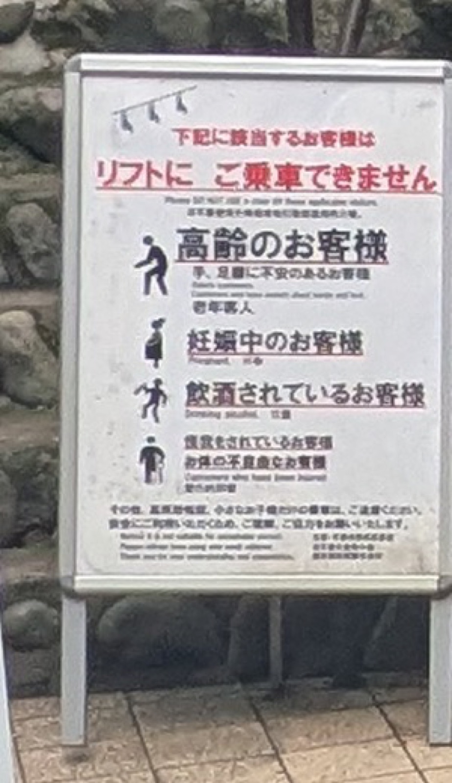 A standing sign at the Mount Takao chairlift with red Japanese text, pictograms listing who may not ride