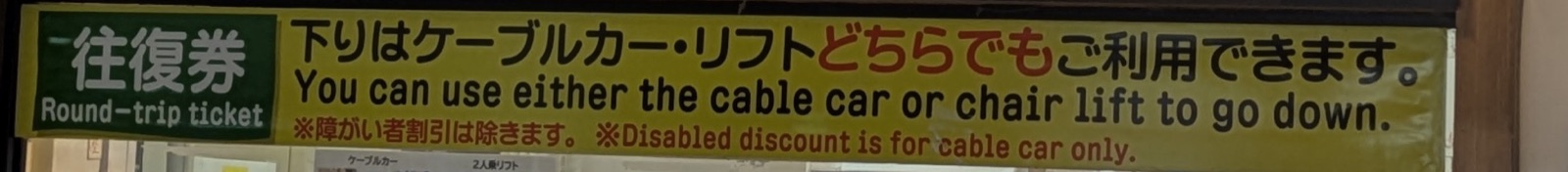 A yellow banner at the Mount Takao ticket office stating in English that a return ticket may be used on either service for the descent