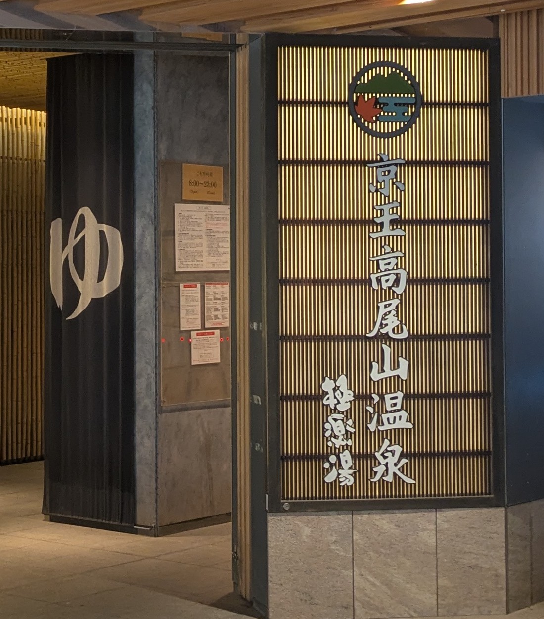 The backlit signboard of Keio Takaosan Onsen Gokurakuyu beside the doorway curtain