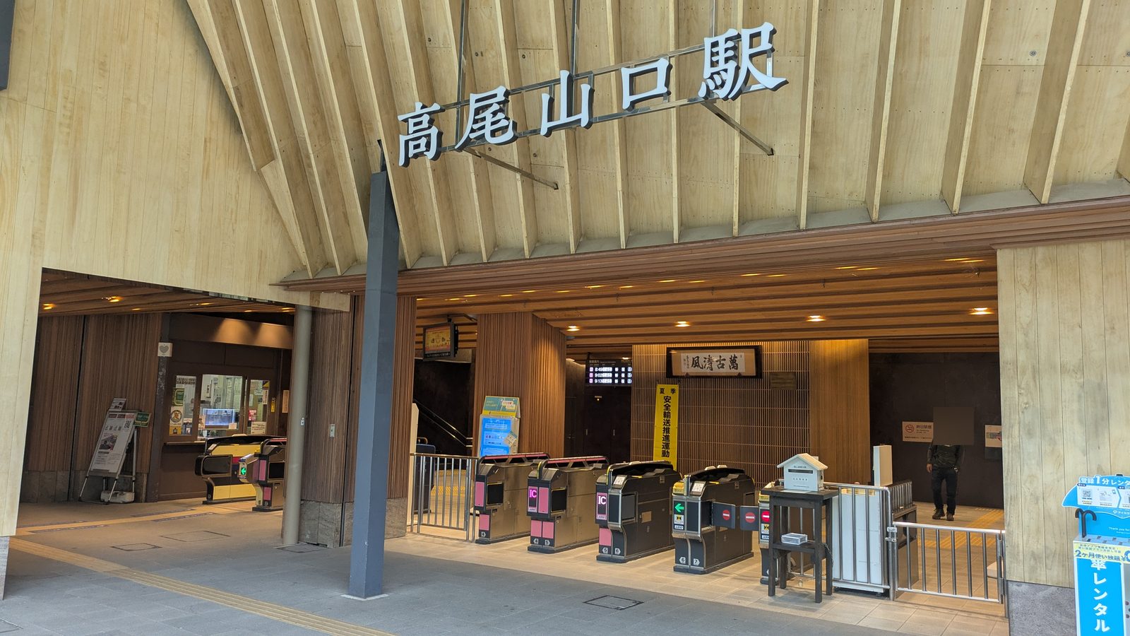 The ticket gates at Takaosanguchi Station with the wooded mountain visible outside