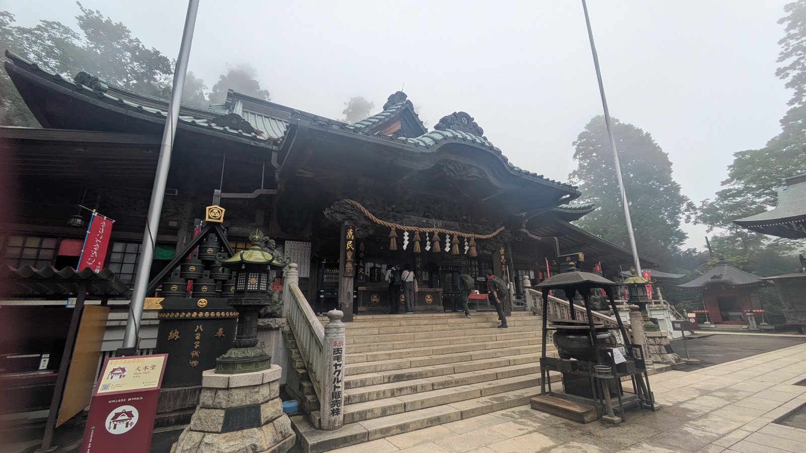 The Main Hall of Takao-san Yakuo-in seen from the courtyard, with a large straw rope above the entrance and an incense burner in front of the steps