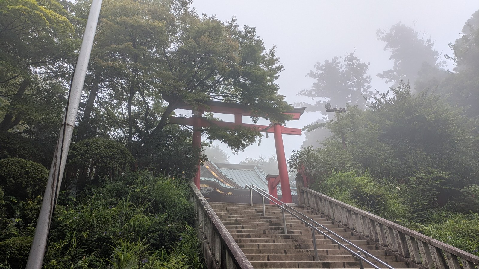 A steep flight of stone steps with handrails climbing through a red torii gate toward a temple hall in mist
