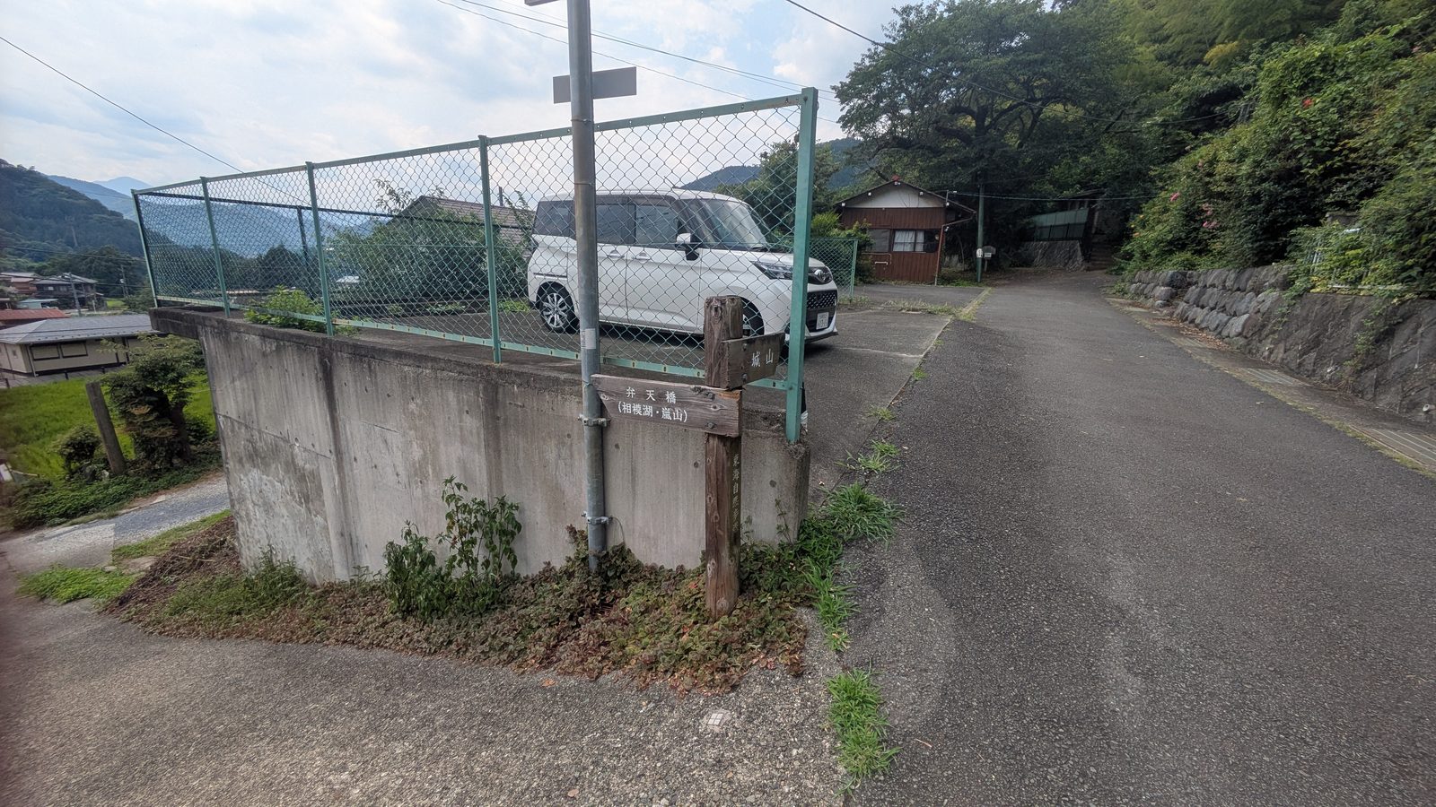 A narrow concrete lane meeting a junction beside a retaining wall with a wooden signpost