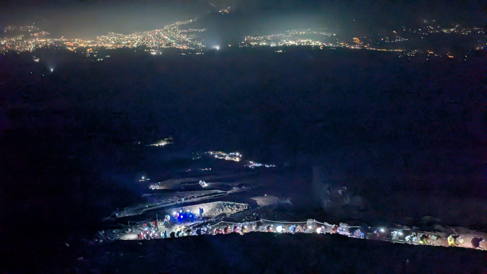 A line of headlamps threading up the dark slope below the eighth station