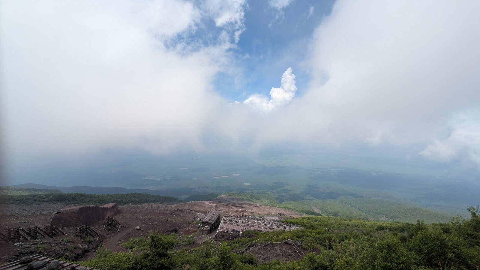 Mountain huts on a red volcanic slope with cloud rising