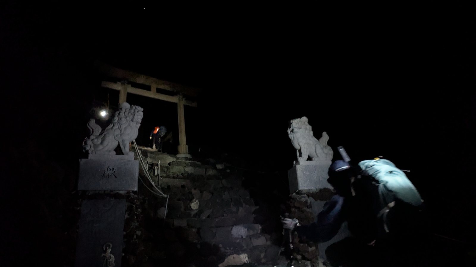 A stone torii at the summit with a pair of guardian lions in darkness
