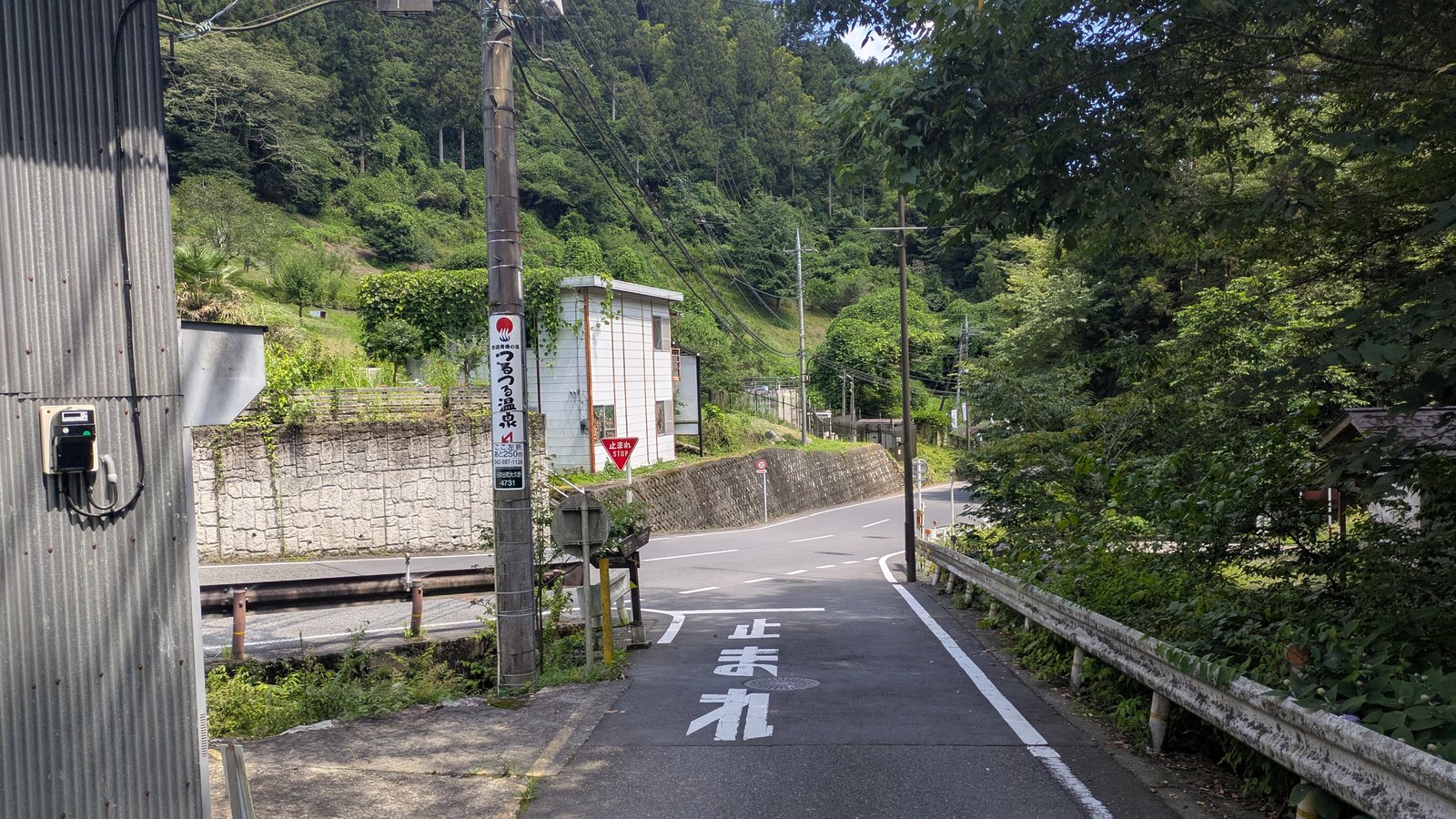 A quiet paved mountain road with a guard rail and a vertical banner sign on a utility pole