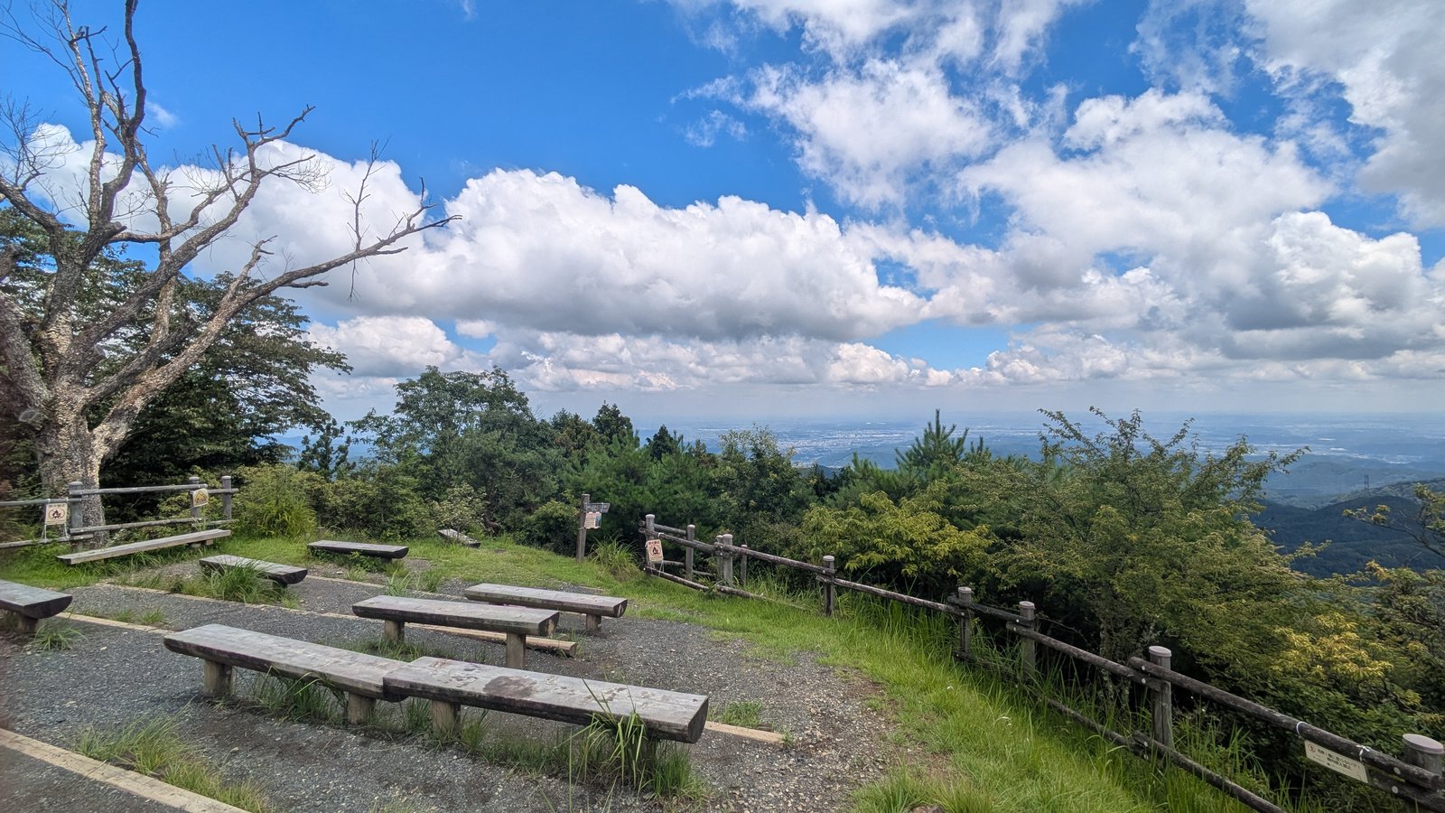 Several long wooden benches on open ground at a mountain summit facing a distant plain under a blue sky