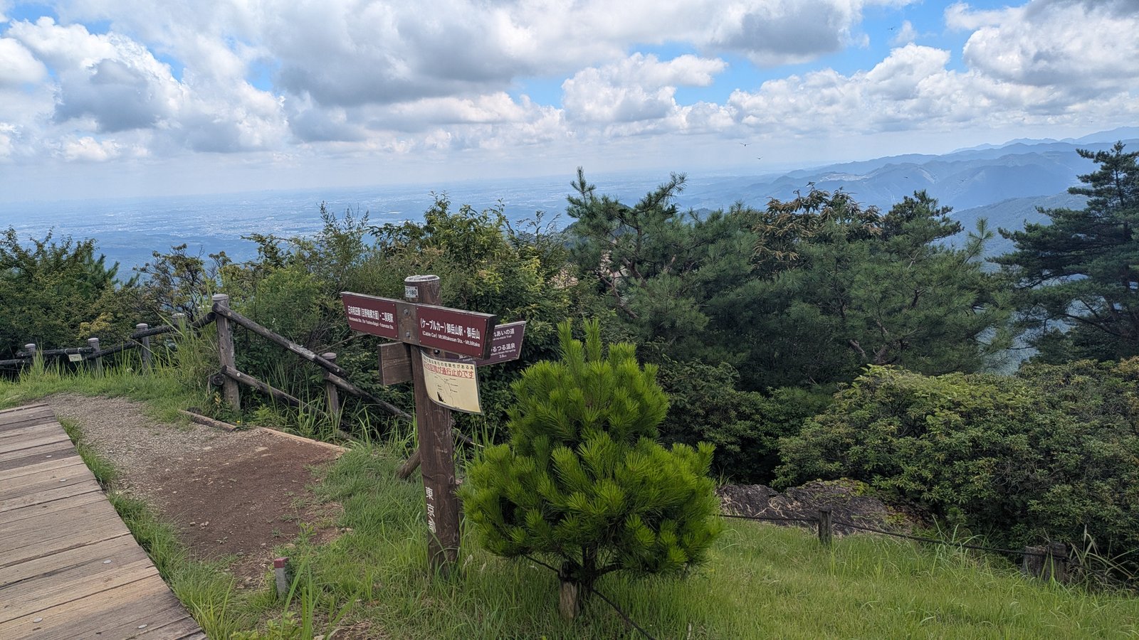A brown wooden signpost at a mountain summit with bilingual Japanese and English destination boards