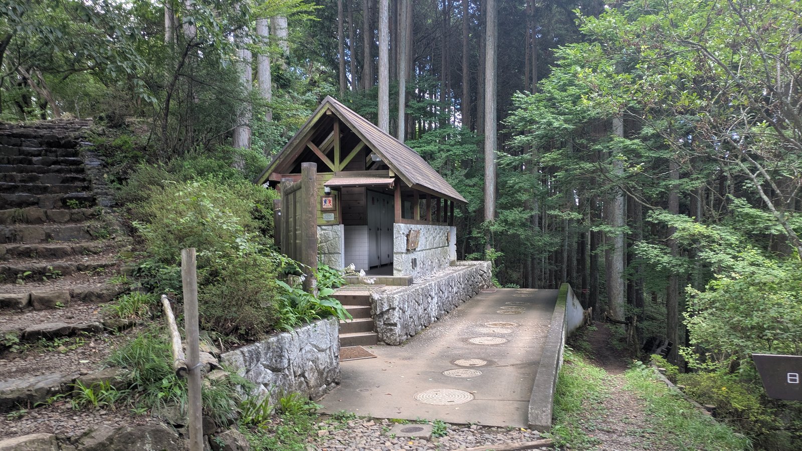 A small wooden toilet building beside a mountain trail among trees