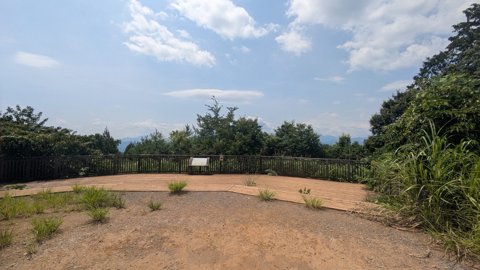 A viewing deck with a metal railing at the end of a broad earth clearing looking out over hills
