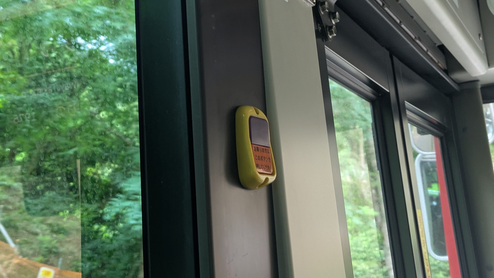 A yellow stop request button mounted on the window pillar of a bus