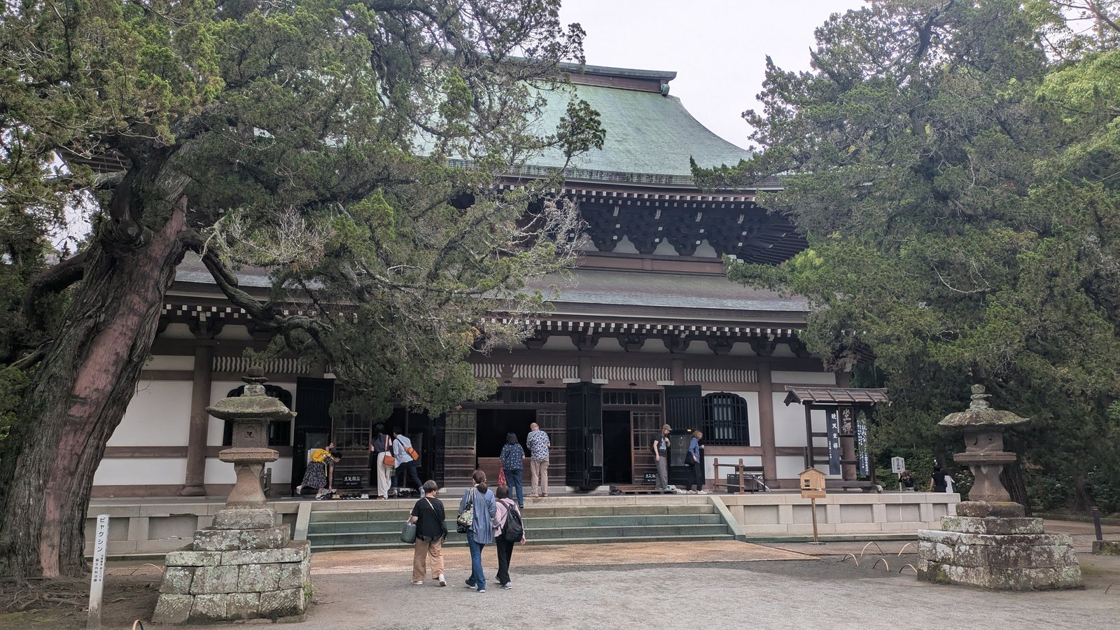 A large wooden temple hall with a tiled roof behind a flat gravel forecourt