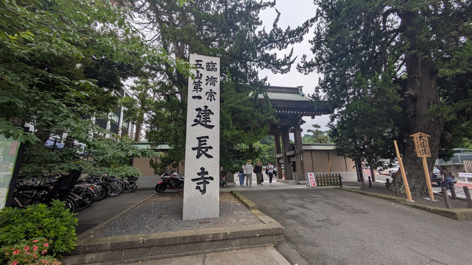 A tall stone pillar carved with the temple name beside a road with parked bicycles