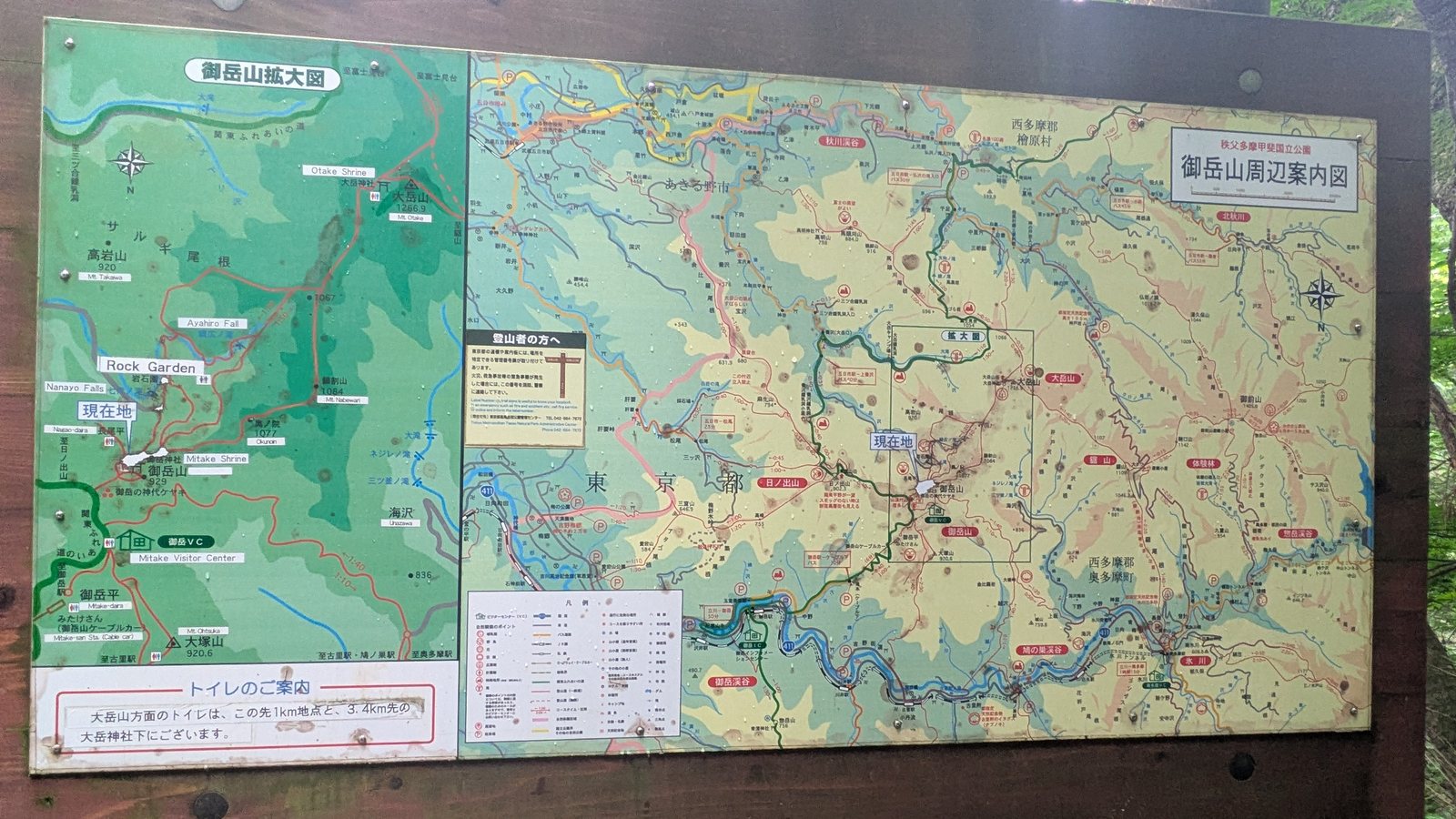 A large national park map board mounted on a wooden frame beside a mountain trail junction
