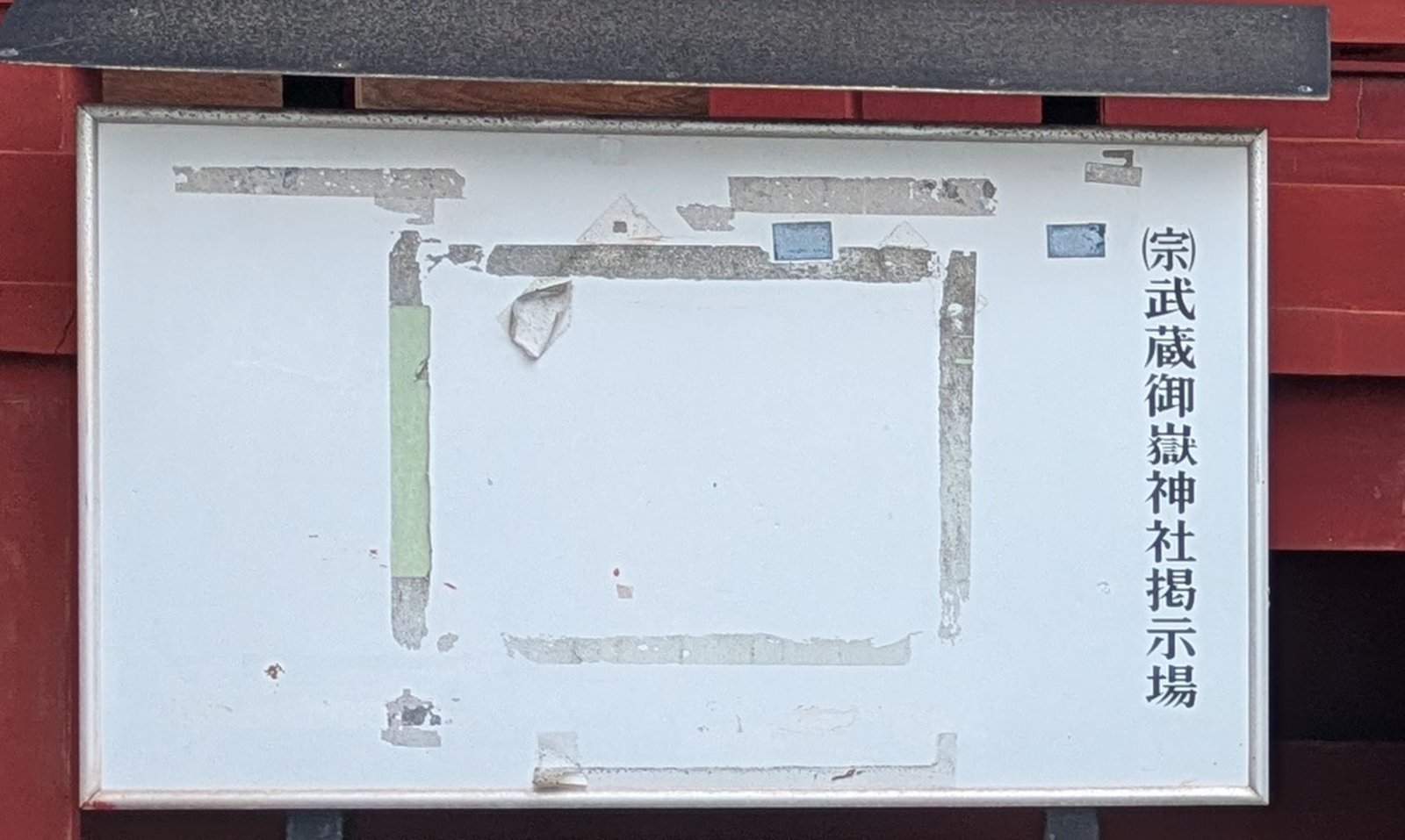 An empty white notice board in a wooden frame at a shrine with only tape marks on it