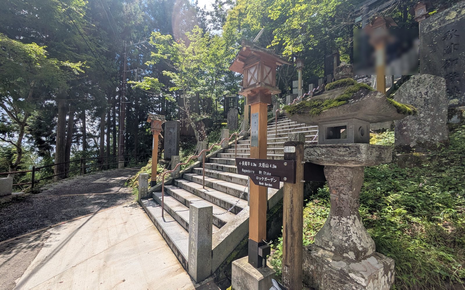 A wooden trail marker post beside long stone steps lined with stone lanterns