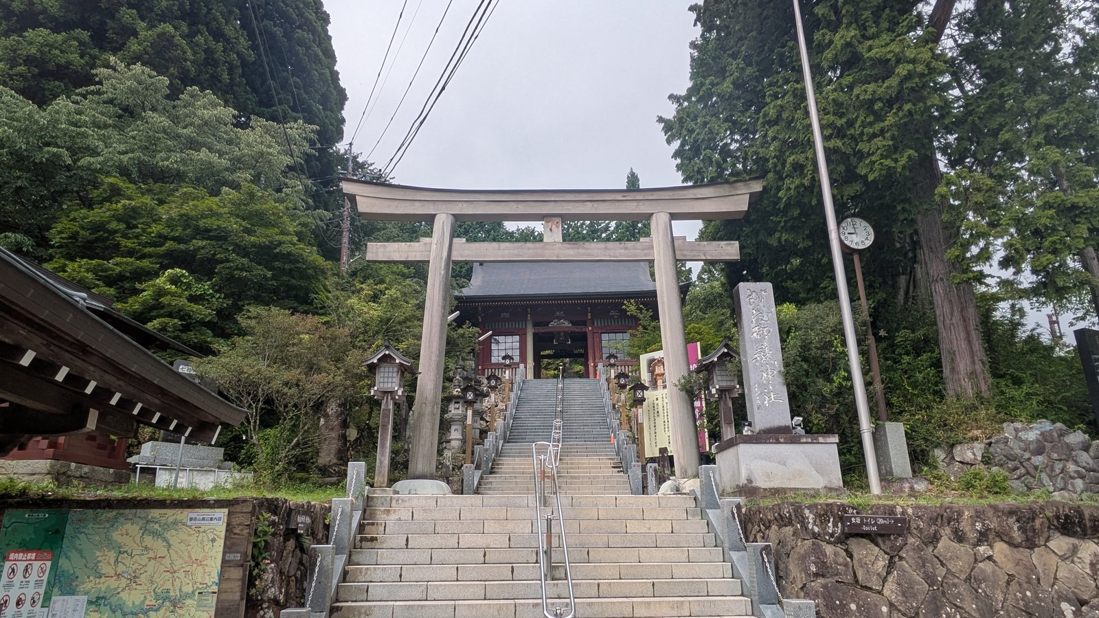 A stone torii gate at the foot of a mountain path with stone lanterns beside it