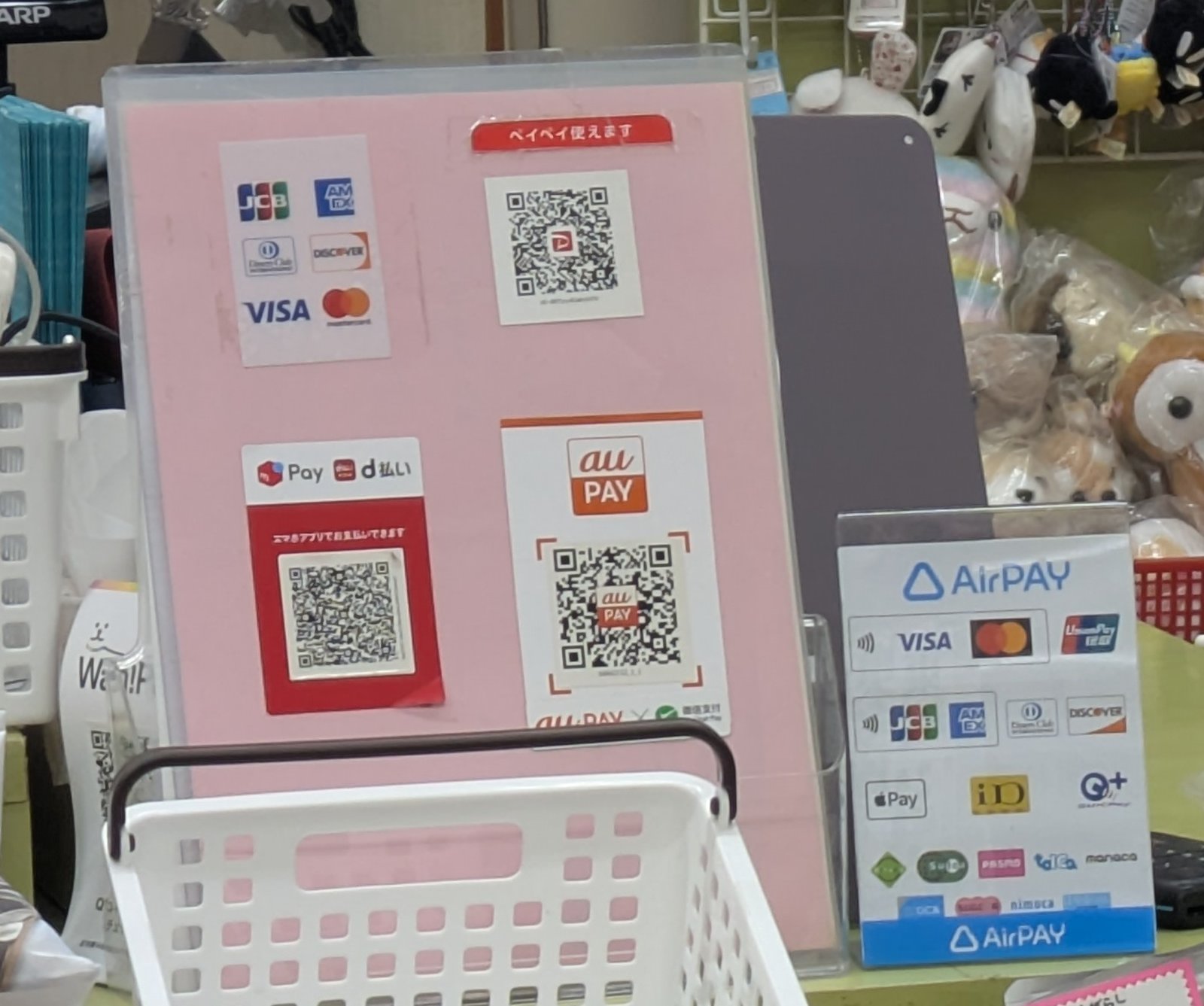 A panel of payment stickers beside a shop counter showing credit card plus QR payment logos