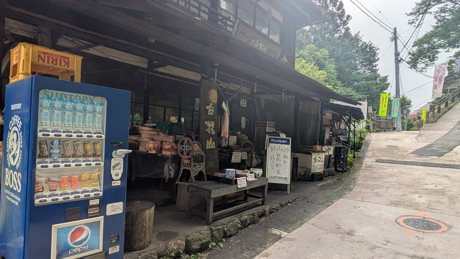 A drinks vending machine standing in front of an old wooden shop on a village lane