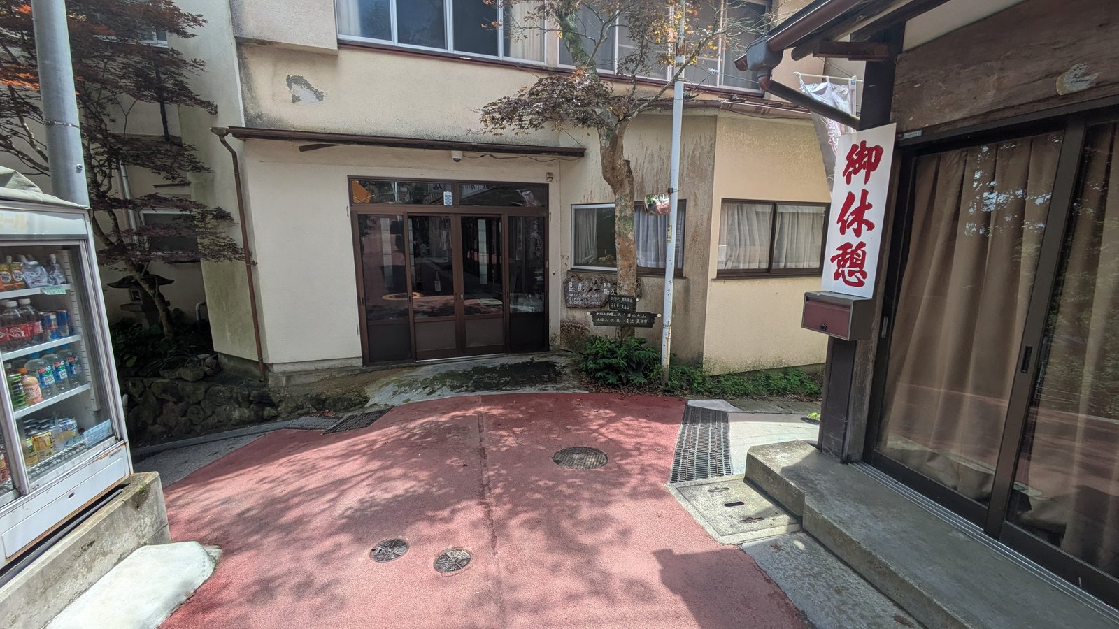 A weathered hand-painted wooden signpost on a village wall listing mountain destinations in Japanese