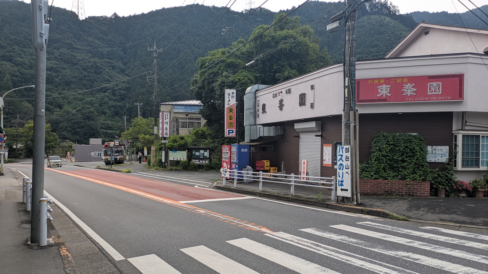 A red bus at a rural bus stop under a brown sign reading For Mt Mitake BUS STOP