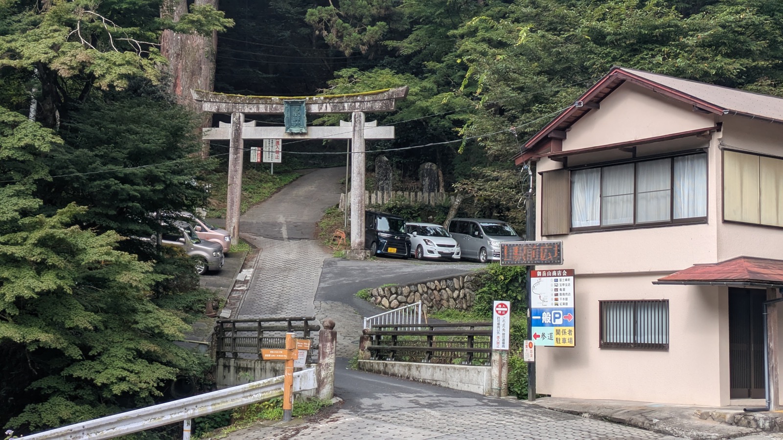 A stone torii gate over a closed lane climbing into cedar forest