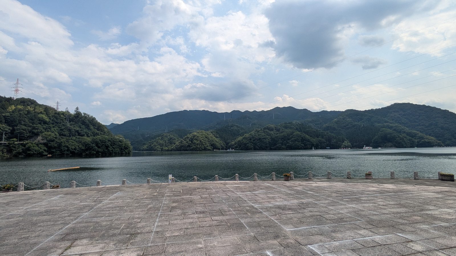 A wide paved lakeside terrace looking out over a lake enclosed by green hills