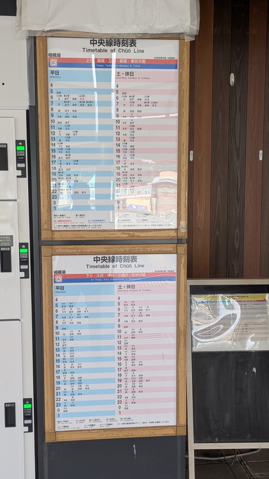 Two JR timetable boards mounted on a wall at a small station with Japanese text alongside English headings