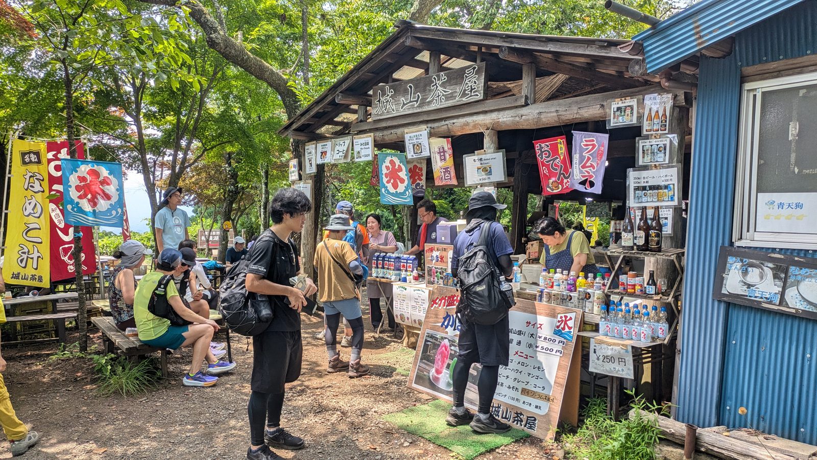 Hikers standing at an open-air mountain teahouse hung with printed banners