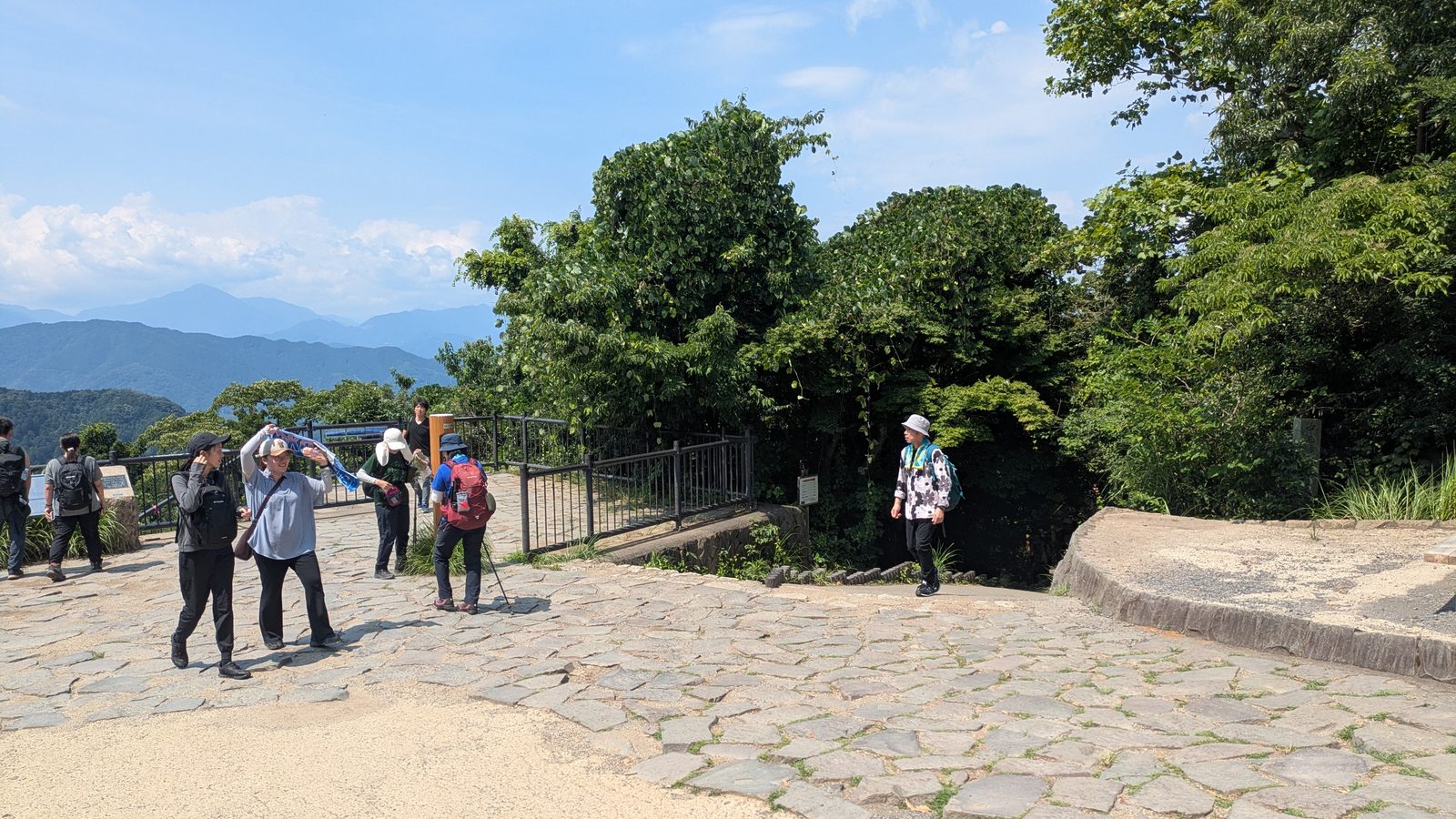 A busy paved summit area crossed by hikers with blue mountains visible beyond