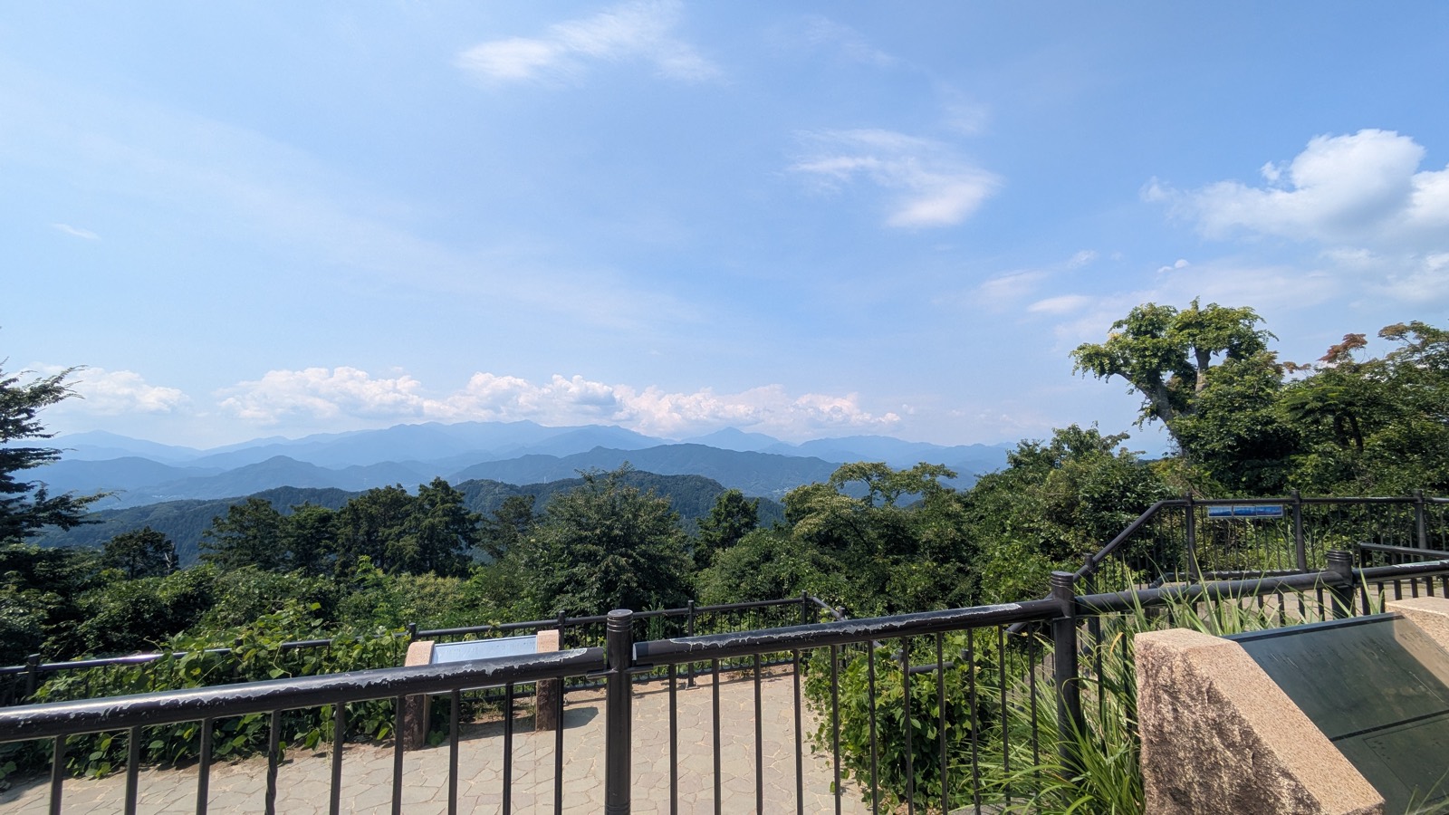 A viewing terrace with railings looking west over layered blue mountain ridges under a summer sky