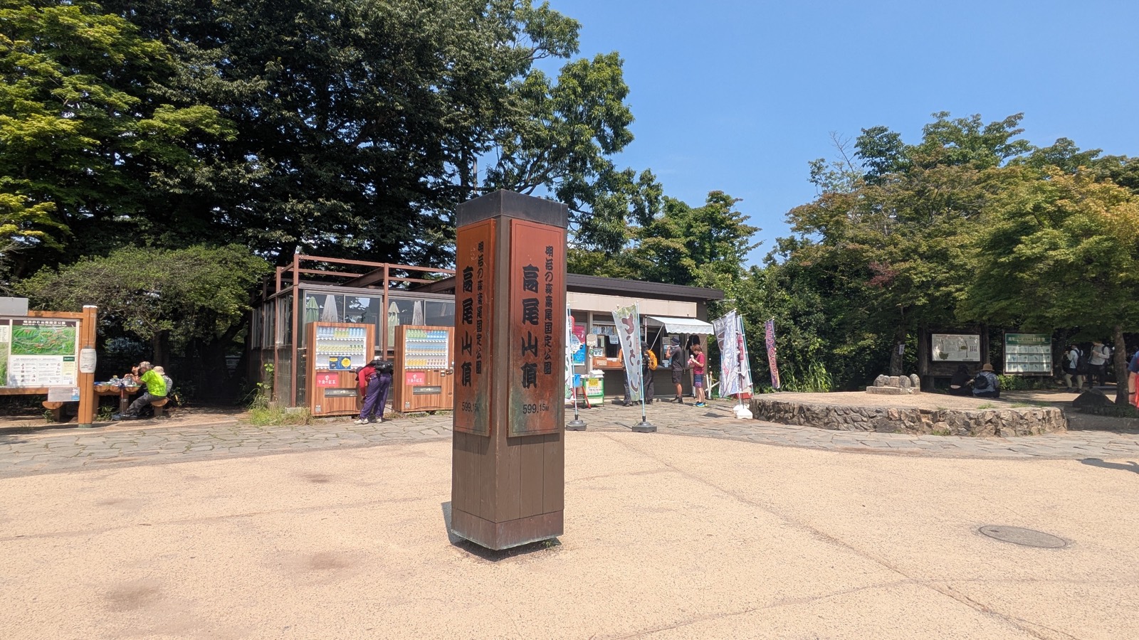 A stone summit marker on a broad open plateau with shops behind it under a blue sky