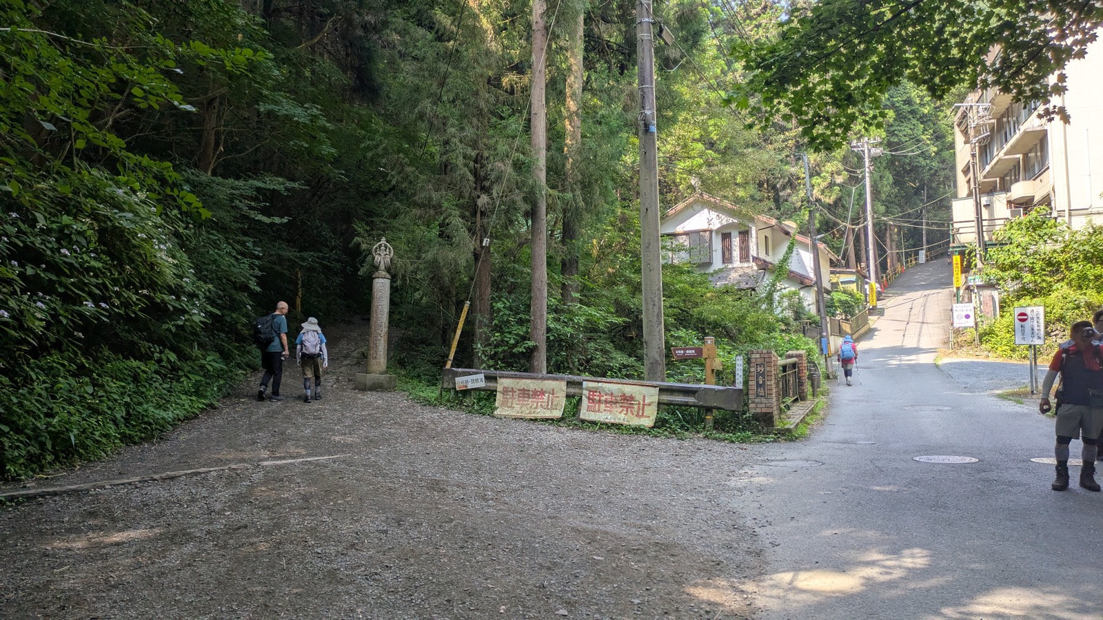 A gravel trail on the left beside a stone pillar with a paved road climbing to the right