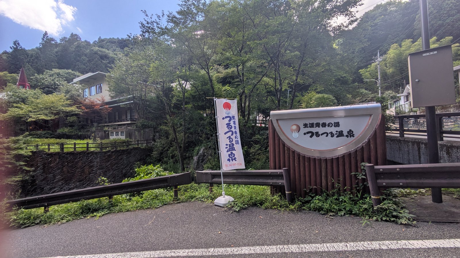 The exterior of a Japanese day-bathhouse building with a tiled roof surrounded by wooded hills