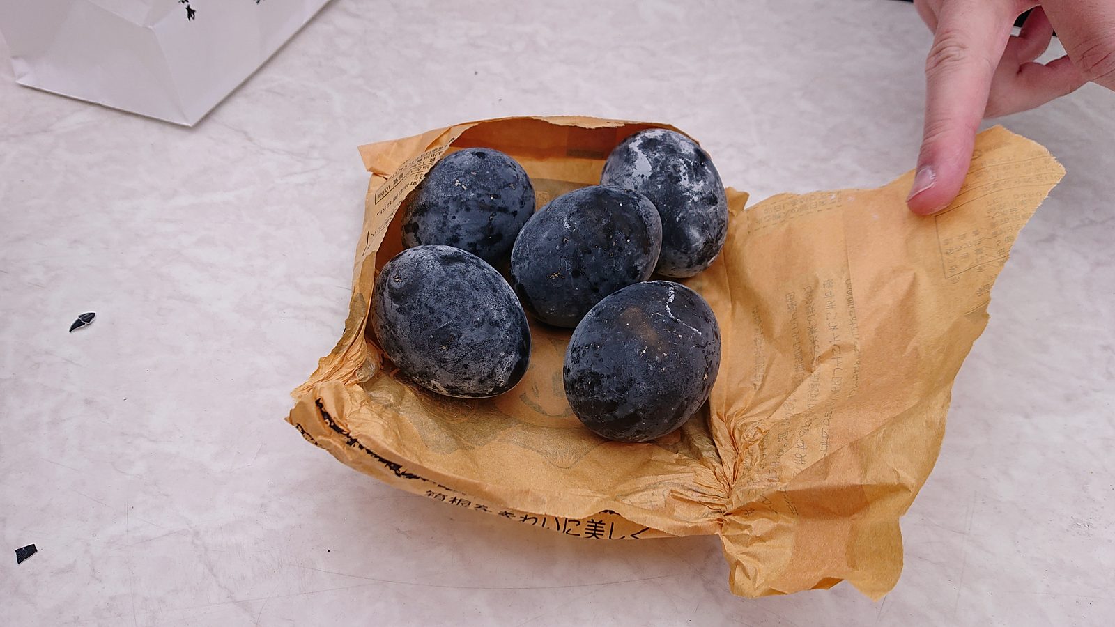 Five black-shelled boiled eggs on a sheet of brown paper, held open by a hand