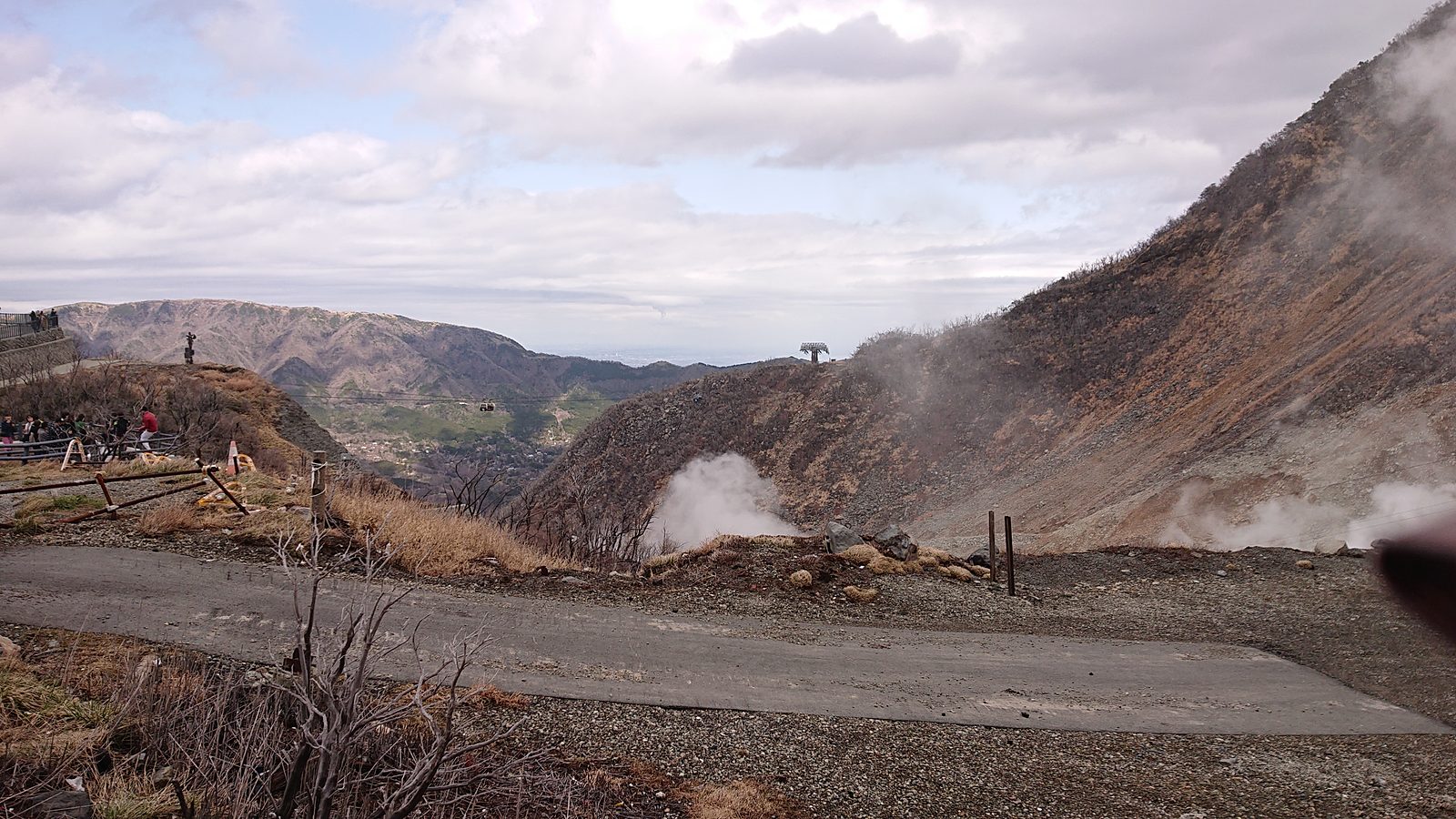 A paved viewing area on a bare volcanic slope at Owakudani, with steam rising from vents on both sides