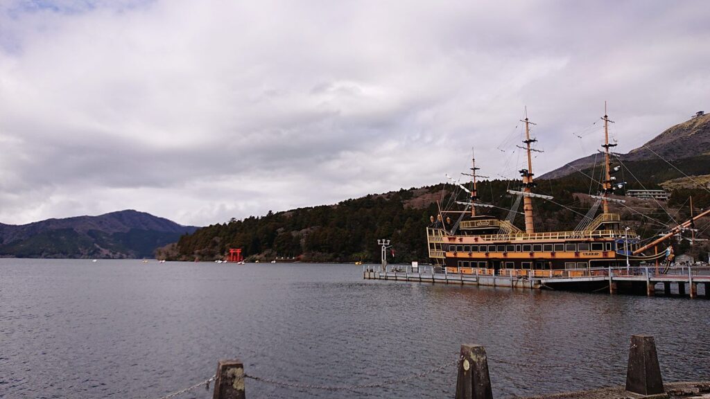 A pirate-style sightseeing ship moored at a pier on Lake Ashi, with a red torii gate on the far shore