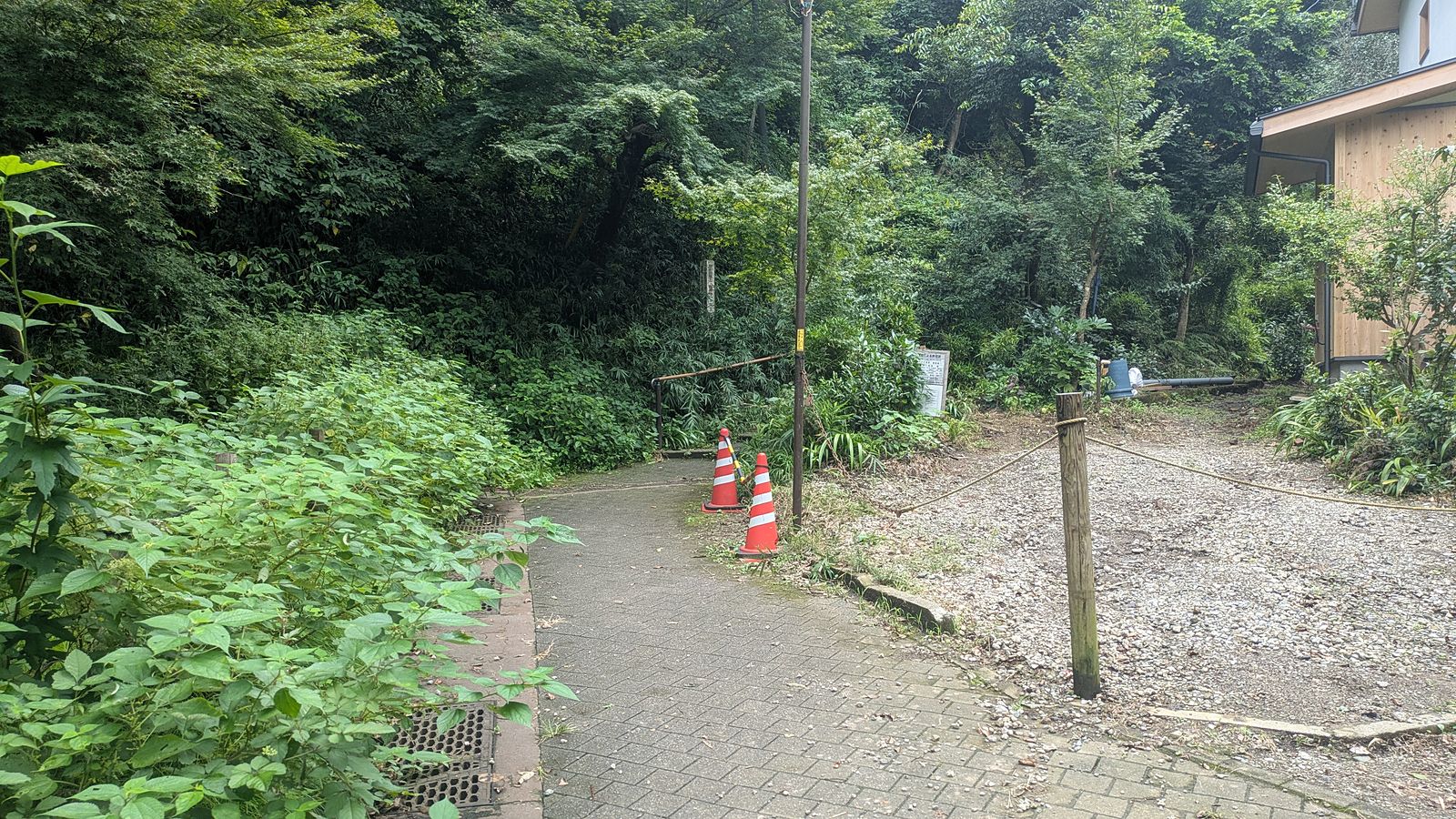 A paved lane ending at a gravel parking area with two traffic cones and wooded hill behind
