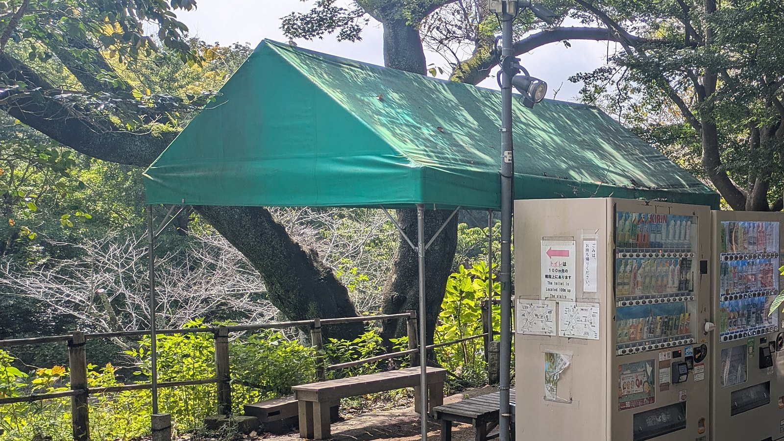 Vending machines under a green awning beside a bench, with a notice about the toilet